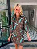 A woman wearing a brown denim zip-front jacket and matching mini skirt set with a vibrant blue and green peacock bird print.