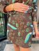A woman wearing a brown denim mini skirt set with a vibrant blue and green peacock bird print.