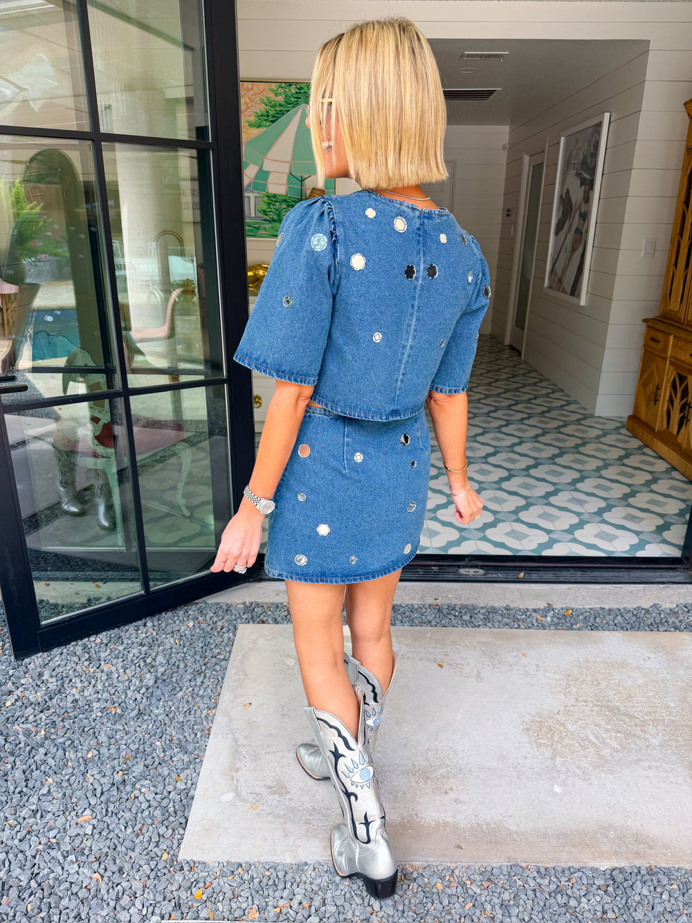 A woman modeling a blue denim short-sleeve top and matching mini skirt set, both decorated with mirror sequin embellishments. Wear this denim set to a concert, date night or gameday.