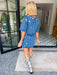 A woman modeling a blue denim short-sleeve top and matching mini skirt set, both decorated with mirror sequin embellishments. Wear this denim set to a concert, date night or gameday.