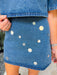 A woman modeling a blue denim short-sleeve top and matching mini skirt set, both decorated with mirror sequin embellishments. Wear this denim set to a concert, date night or gameday.