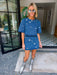 A woman modeling a blue denim short-sleeve top and matching mini skirt set, both decorated with mirror sequin embellishments. Wear this denim set to a concert, date night or gameday.