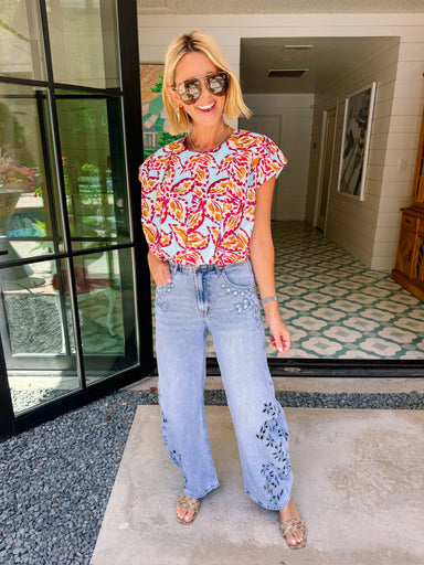 A woman wearing light-wash wide-leg jeans with floral eyelet cutout on the lower legs.