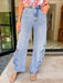 A women wearing light-wash wide-leg jeans with floral embroidery and eyelet cutout details on the outer thighs, paired with a colorful floral top and tan slide sandals. 