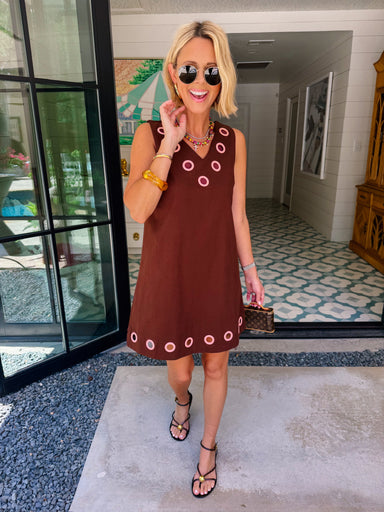 A woman modeling a sleeveless brown dress with circular cutout grommet details along neckline and hem.