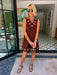 A woman modeling a sleeveless brown dress with circular cutout grommet details along neckline and hem.