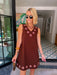 A woman modeling a sleeveless brown dress with circular cutout grommet details along neckline and hem.