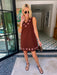 A woman modeling a sleeveless brown dress with circular cutout grommet details along neckline and hem.