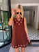 A woman modeling a sleeveless brown dress with circular cutout grommet details along neckline and hem.