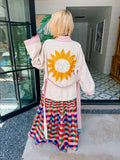 A women viewed from behind wearing a cream-colored jacket with a large beaded yellow sun on the back,