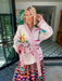 A woman wearing a cream-colored embroidered, beaded kimono-style jacket with pink striped trim and sunshine motif