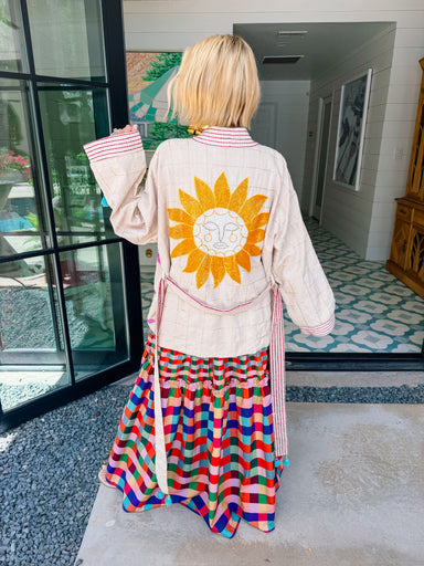 A women viewed from behind wearing a cream-colored jacket with a large beaded yellow sun on the back,
