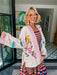 A woman wearing a cream-colored embroidered, beaded kimono-style jacket with pink striped trim and sunshine motif