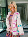 A woman wearing a cream-colored embroidered, beaded kimono-style jacket with pink striped trim and sunshine motif