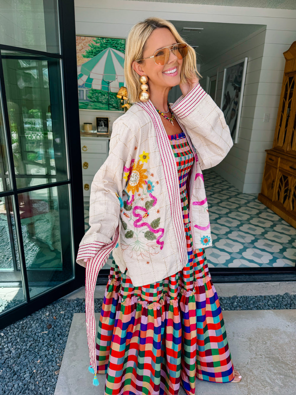 A woman wearing a cream-colored embroidered, beaded kimono-style jacket with pink striped trim and sunshine motif
