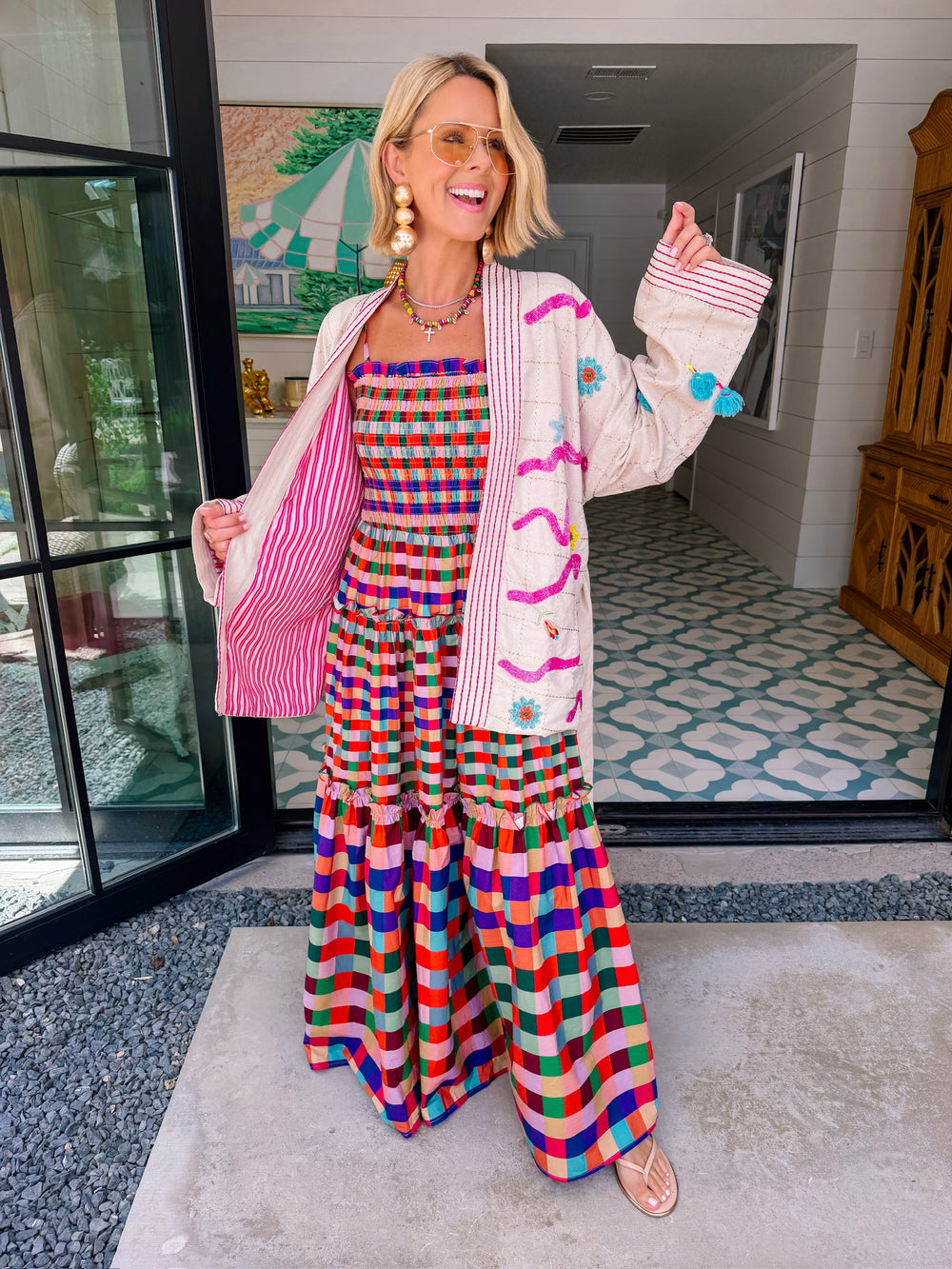A woman wearing a cream-colored embroidered, beaded kimono-style jacket with pink striped trim and sunshine motif