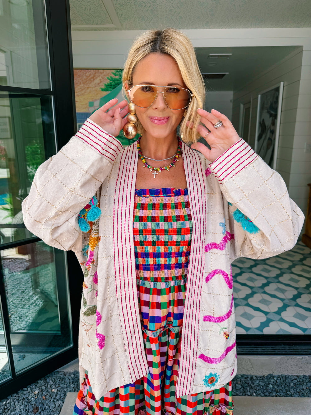 A woman wearing a cream-colored embroidered, beaded kimono-style jacket with pink striped trim and sunshine motif