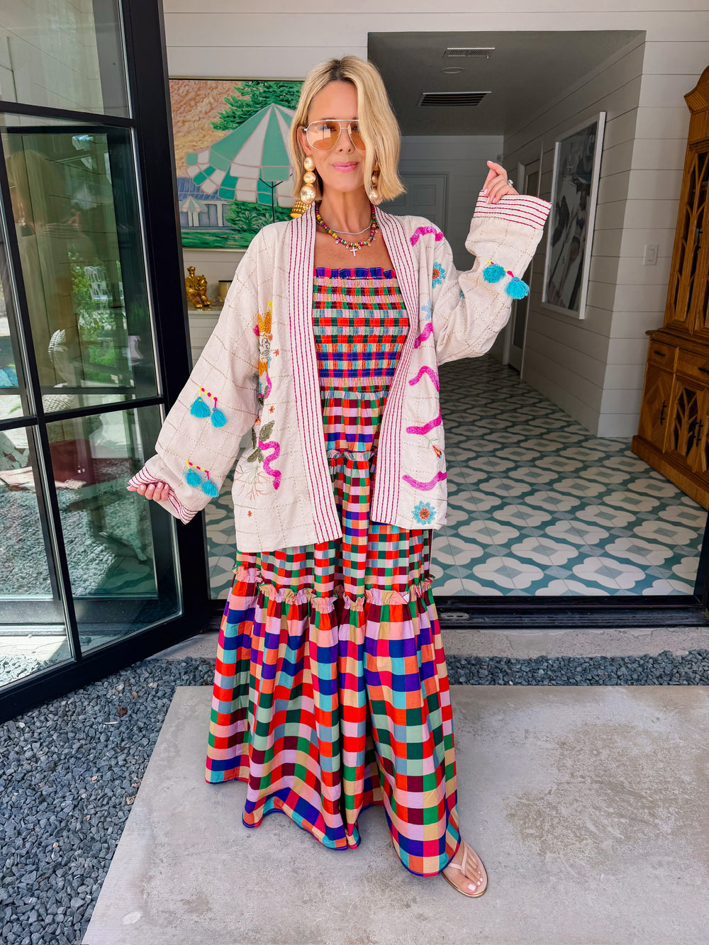 A woman wearing a cream-colored embroidered, beaded kimono-style jacket with pink striped trim and sunshine motif
