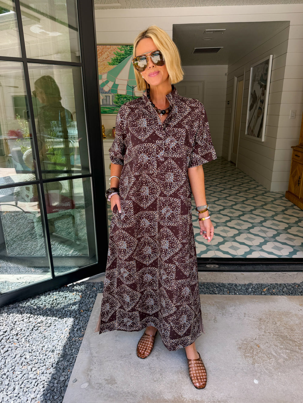 A woman wearing a brown and blue bandana patterned maxi shirt dress with short sleeves. Wear to a rodeo or western event.

