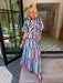 A woman wearing a colorful striped matching set consisting of a short-sleeve collared top and a tiered maxi skirt. The stripe print with blue, white, pink and brown colors, make this a perfect transition piece for summer and fall.

