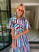 A woman wearing a colorful striped matching set consisting of a short-sleeve collared top and a tiered maxi skirt. The stripe print with blue, white, pink and brown colors, make this a perfect transition piece for summer and fall.