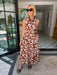 A woman stands in a home entryway wearing a sleeveless brown maxi dress with a white floral pattern. The dress features transition colors for summer and fall.

