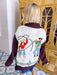 A woman wearing a western, rodeo themed cardigan sweater with brown sleeves. This cardi features cowboys and cowgirls lassoing, doing rope tricks. Perfect for rodeo, FW stockyards, stock show or any western event. Style with denim or over any dress.