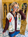 A woman wearing a western, rodeo themed cardigan sweater with brown sleeves. This cardi features cowboys and cowgirls lassoing, doing rope tricks. Perfect for rodeo, FW stockyards, stock show or any western event. Style with denim or over any dress.