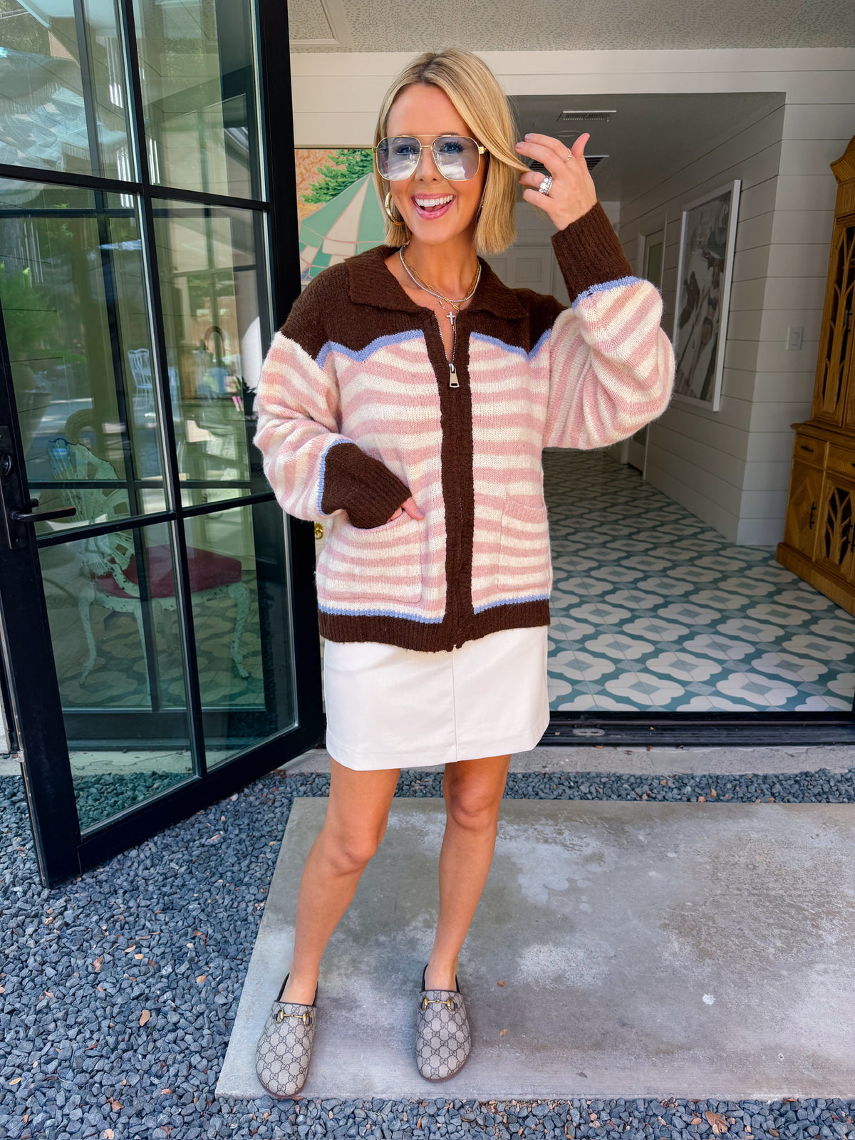 A woman wearing a western cardigan featuring a bronco and cowboy design on the back. This pink and white striped cardigan is perfect for rodeos, western events or country music concerts. Pair with denim or leather skirts.