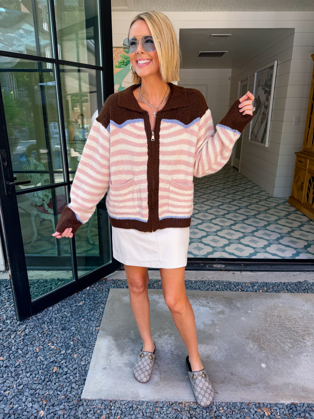 A woman wearing a western cardigan featuring a bronco and cowboy design on the back. This pink and white striped cardigan is perfect for rodeos, western events or country music concerts. Pair with denim or leather skirts.